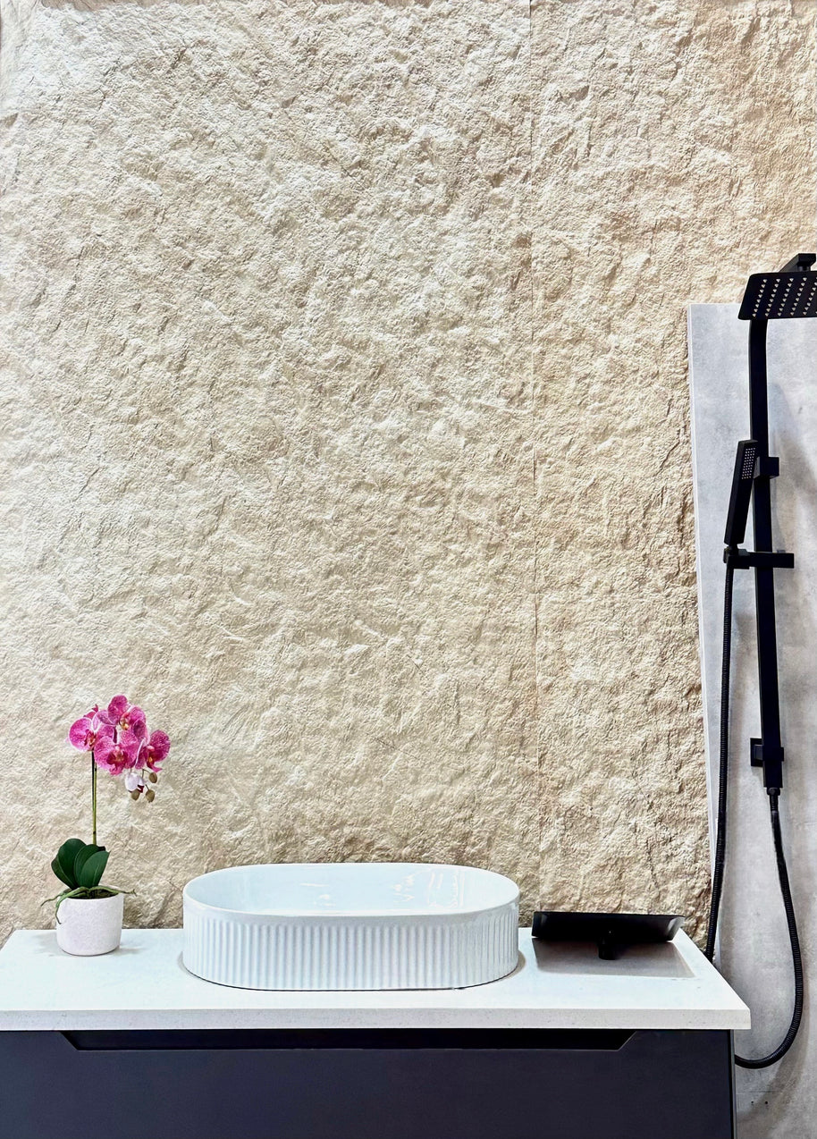 White sink on a vanity with a textured beige wall and a pink orchid in the background.