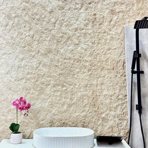 White sink on a vanity with a textured beige wall and a pink orchid in the background.