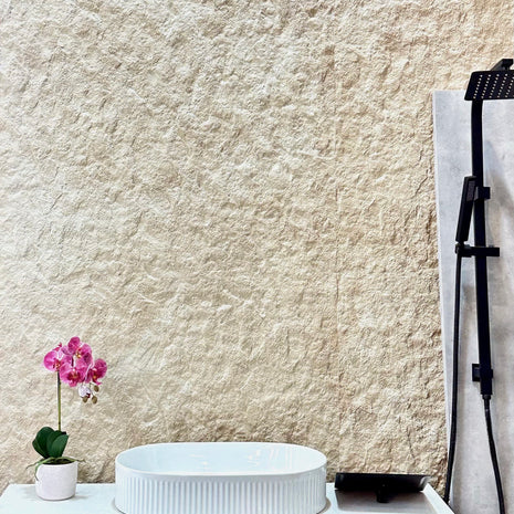 White sink on a vanity with a textured beige wall and a pink orchid in the background.