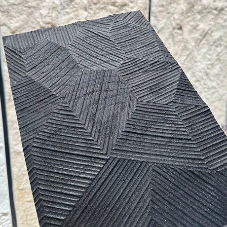 Textured black tile with geometric pattern on a light stone wall background