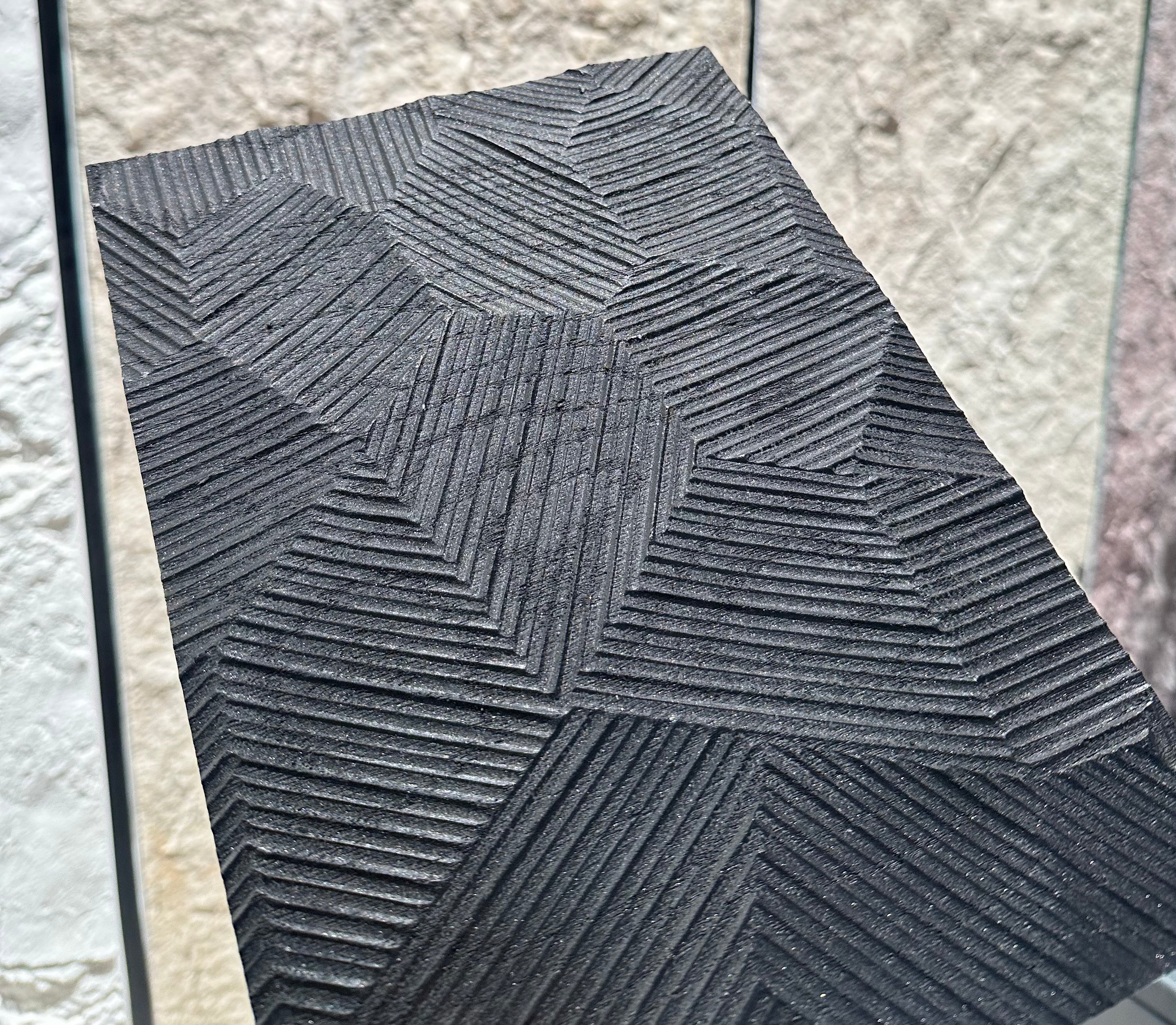 Textured black tile with geometric pattern on a light stone wall background