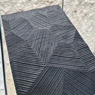 Textured black tile with geometric pattern on a light stone wall background